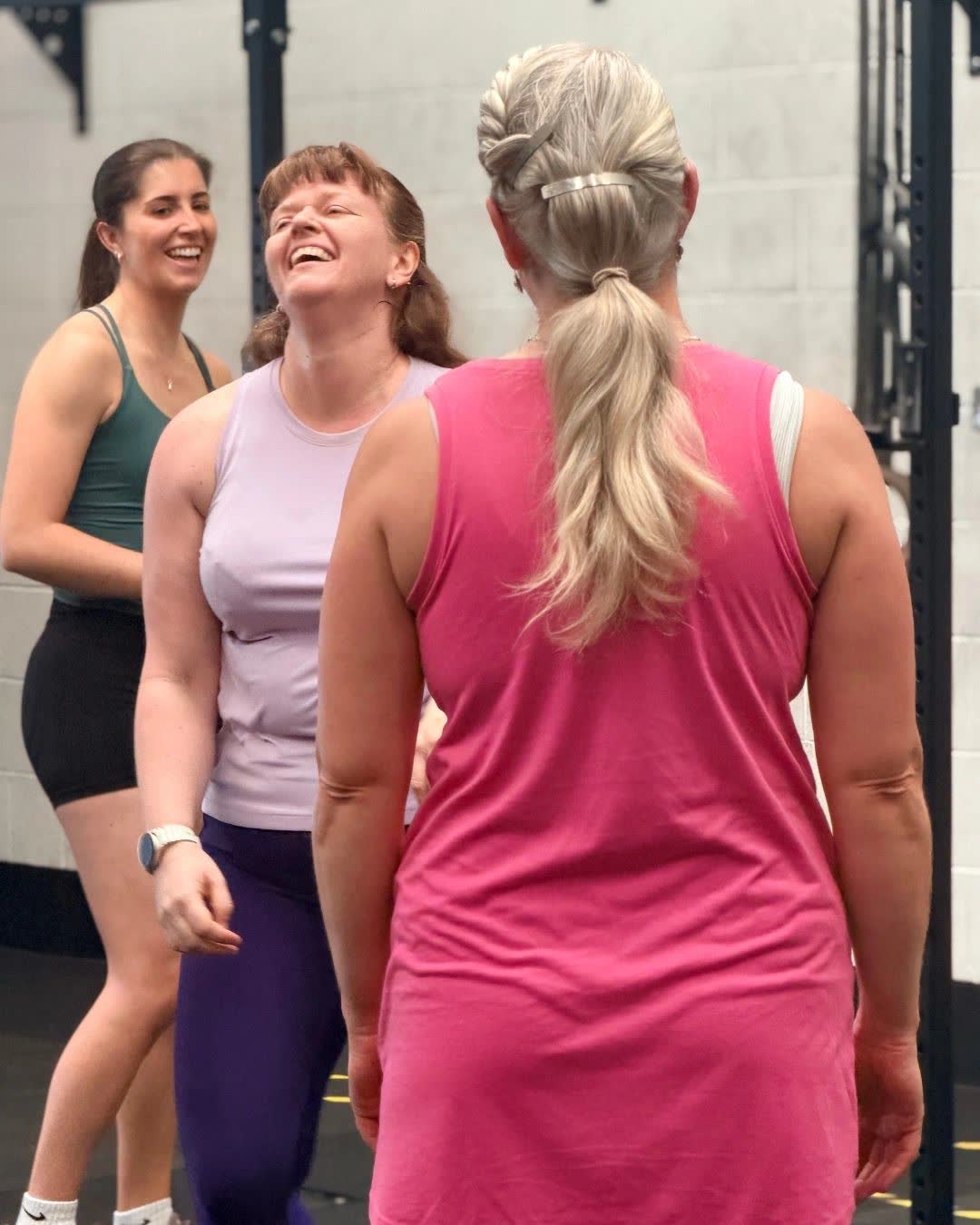 Three women laughing together on the gym floor