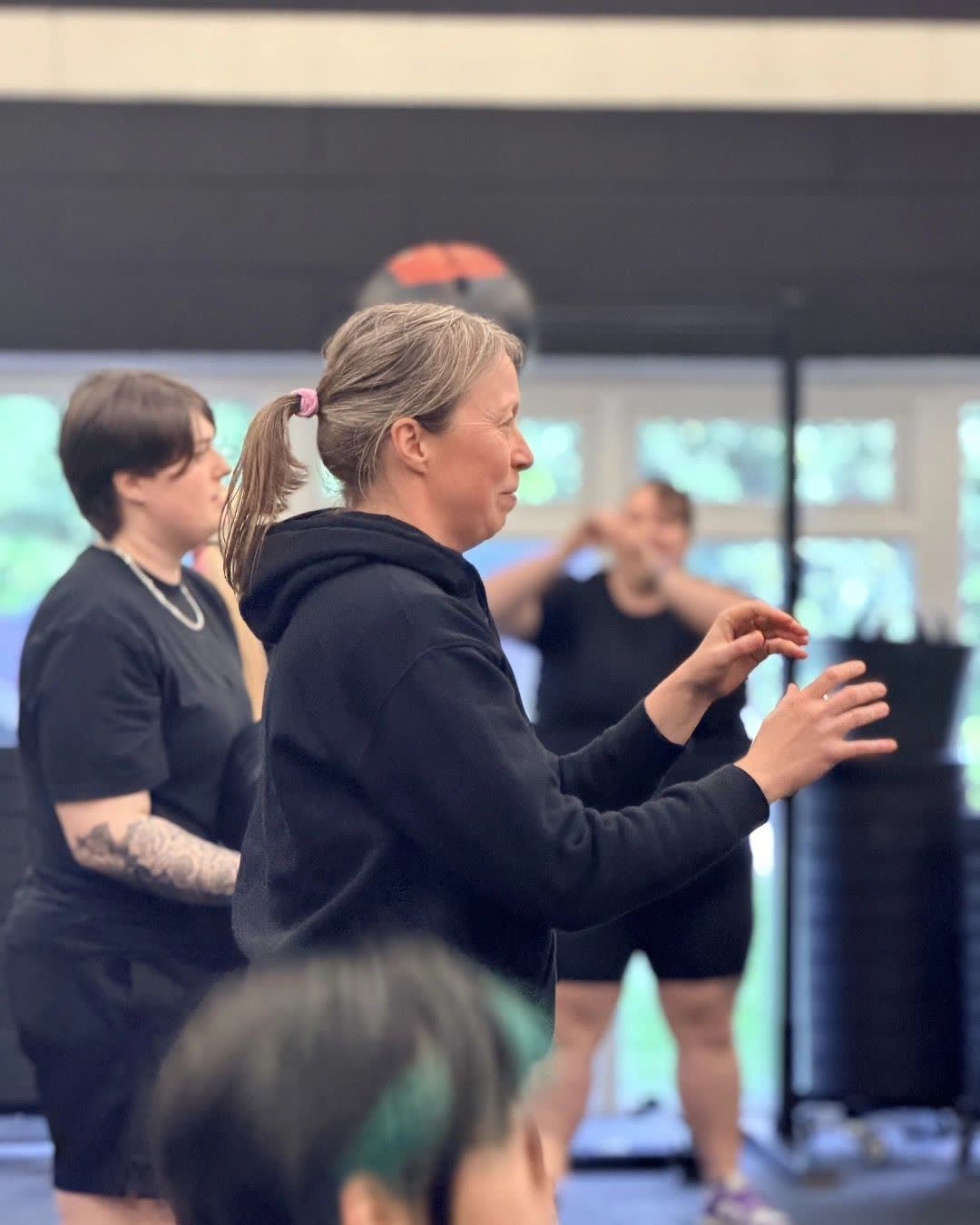 A coach in a black hoodie talking a small group of members through a session