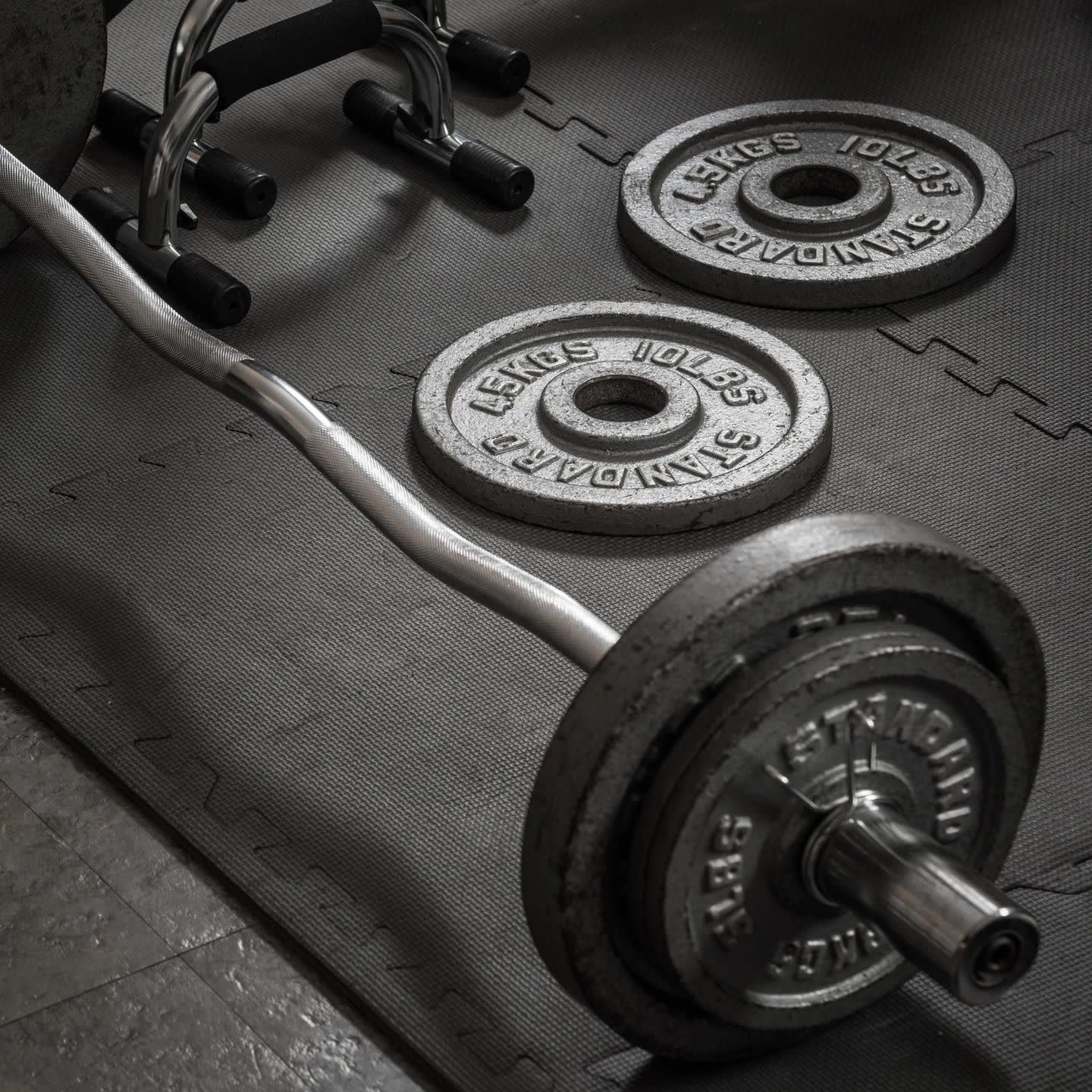 A barbell loaded with iron plates on a gym floor, in black and white