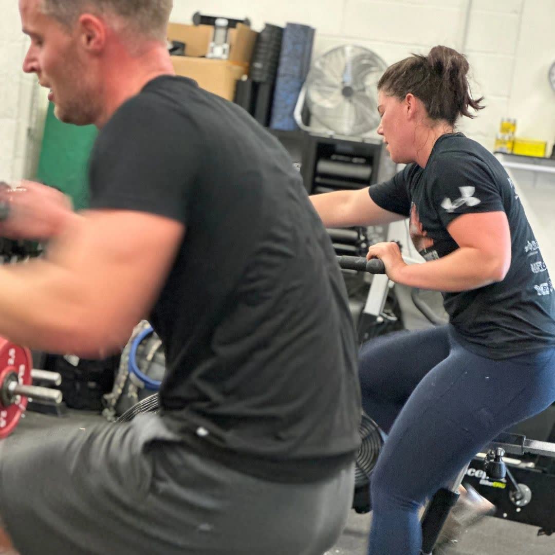 A man and a woman working hard on air bikes side by side