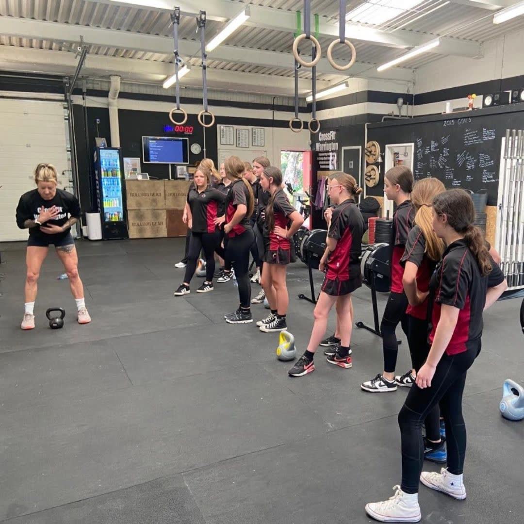 A group of schoolgirls in the gym with kettlebells, listening to a coach