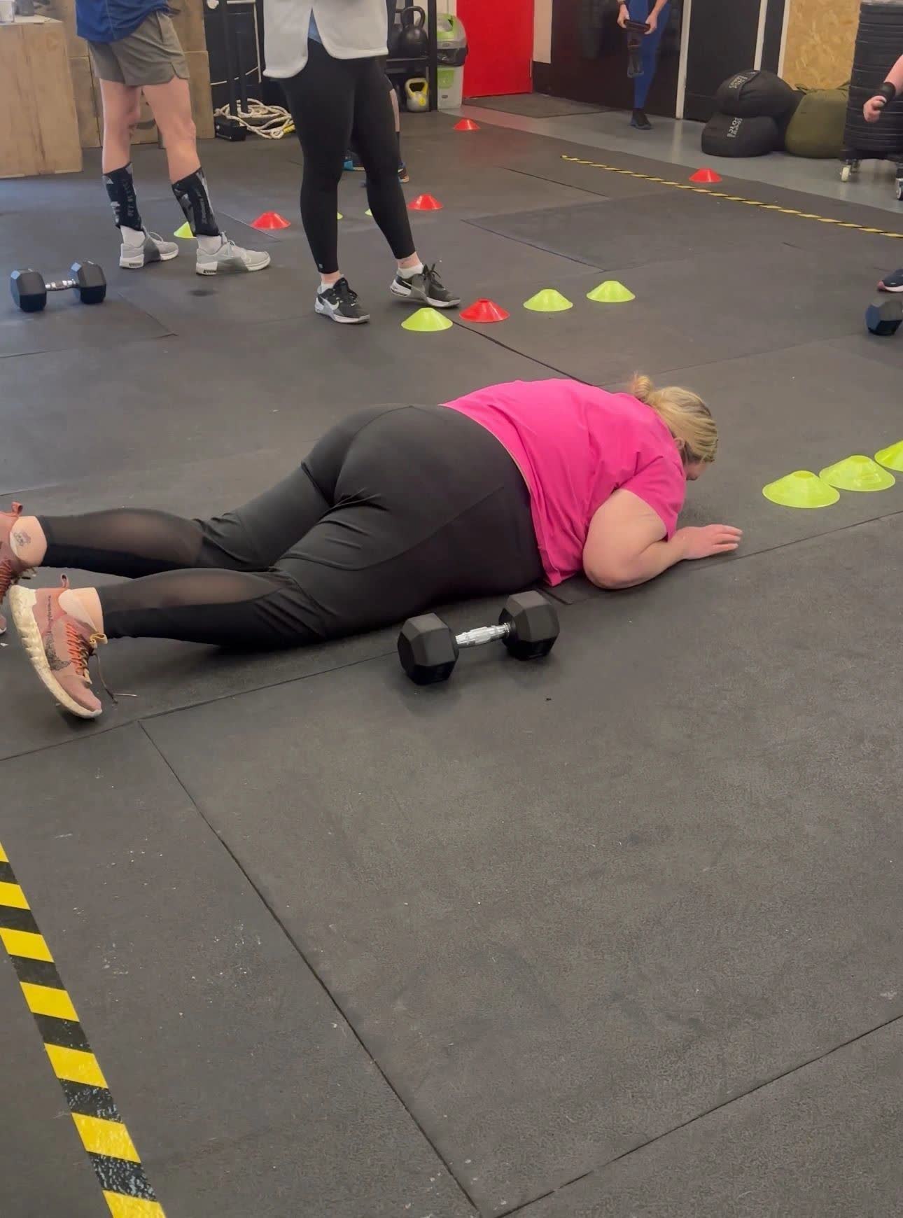 A member lying flat on the gym floor beside her dumbbells after finishing a workout