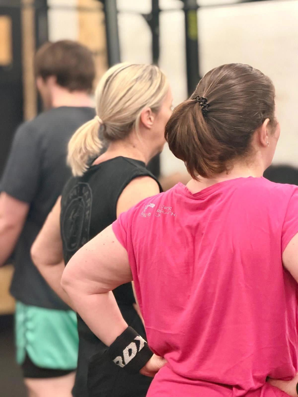 Three members seen from behind, watching a class on the gym floor