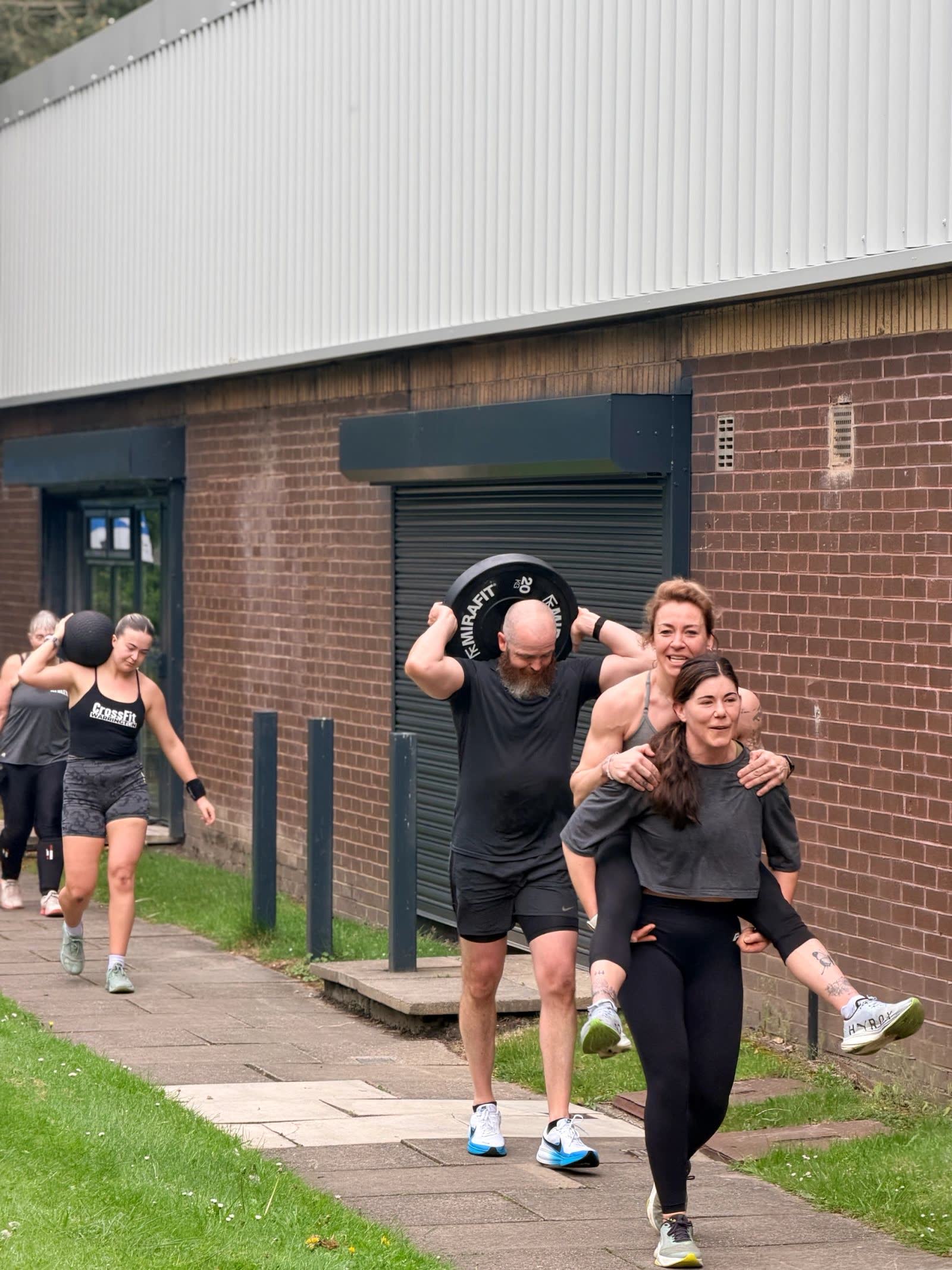 Members carrying weight plates and each other along the path outside the gym