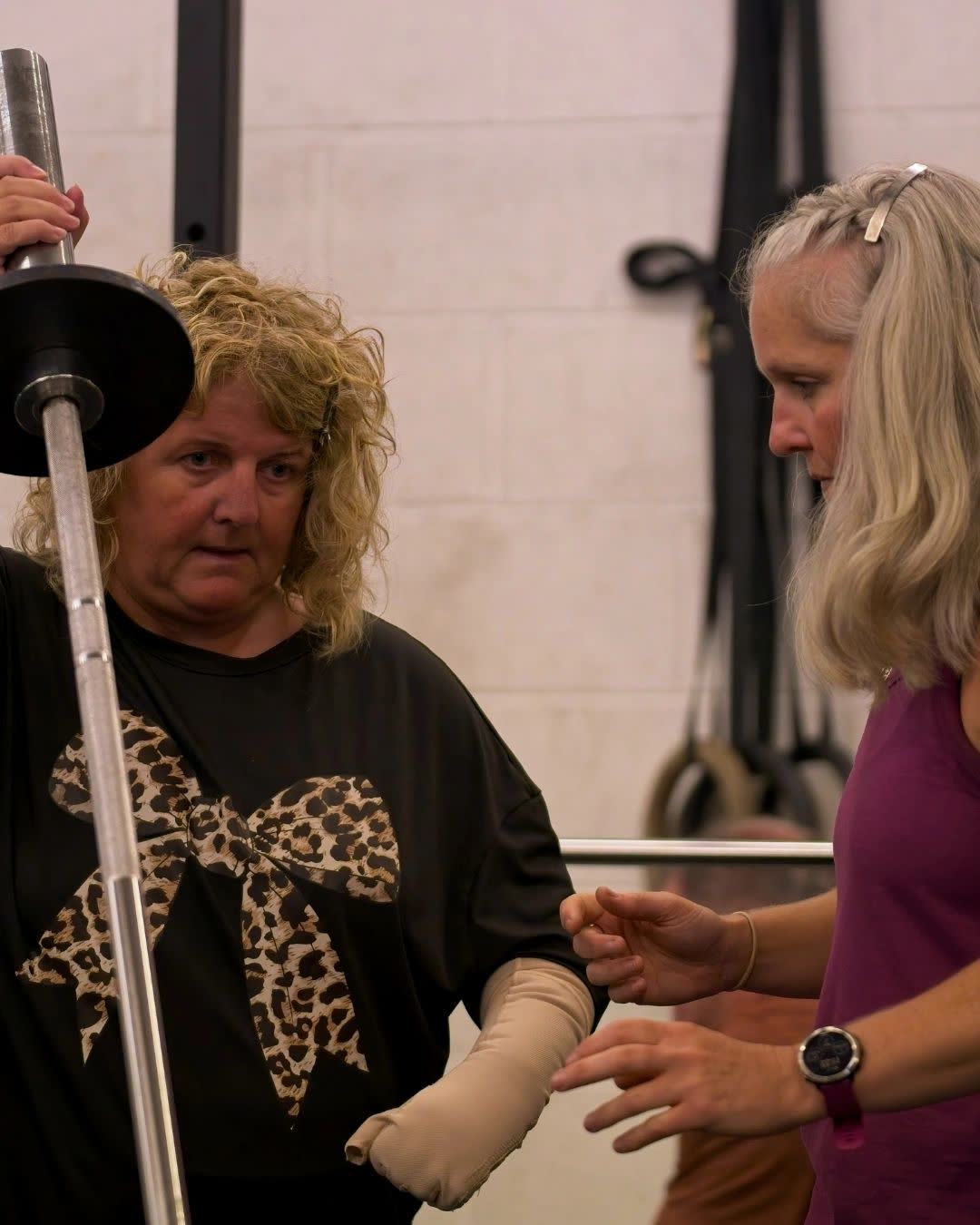 An adaptive athlete lifting a bar with a coach beside her