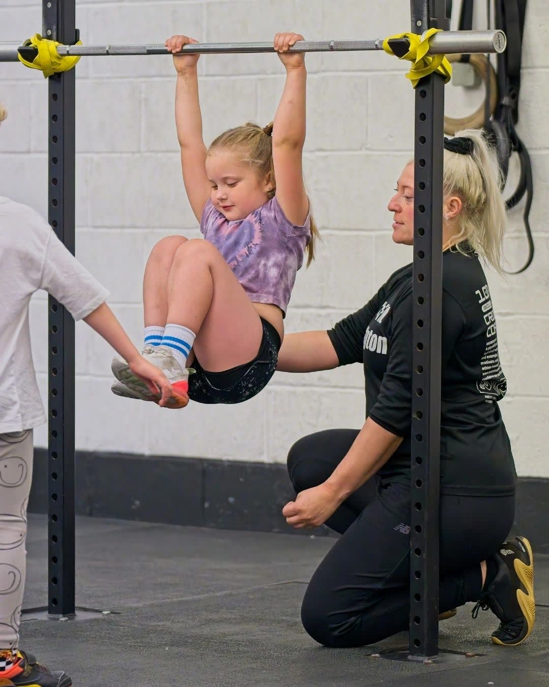 A coach helping a girl hang from a pull-up bar