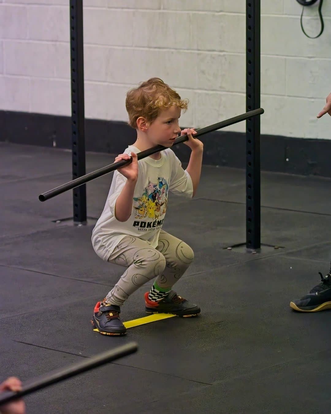 A boy squatting with a light bar on his shoulders