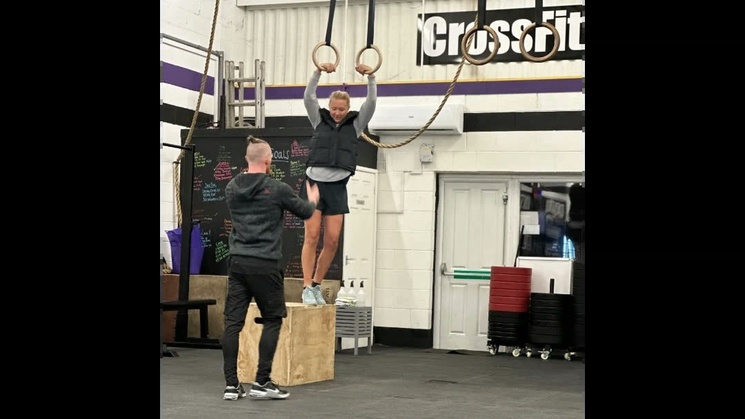 A coach spotting a member on the gymnastic rings