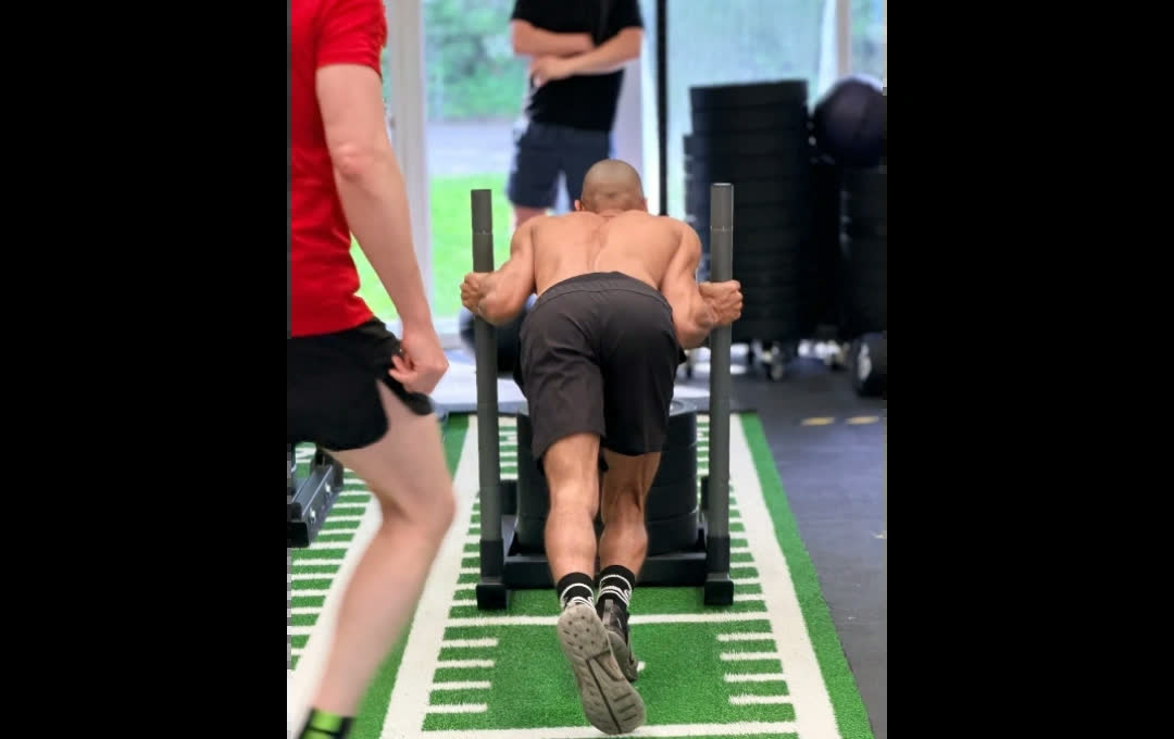 An athlete pushing a weighted sled along the turf