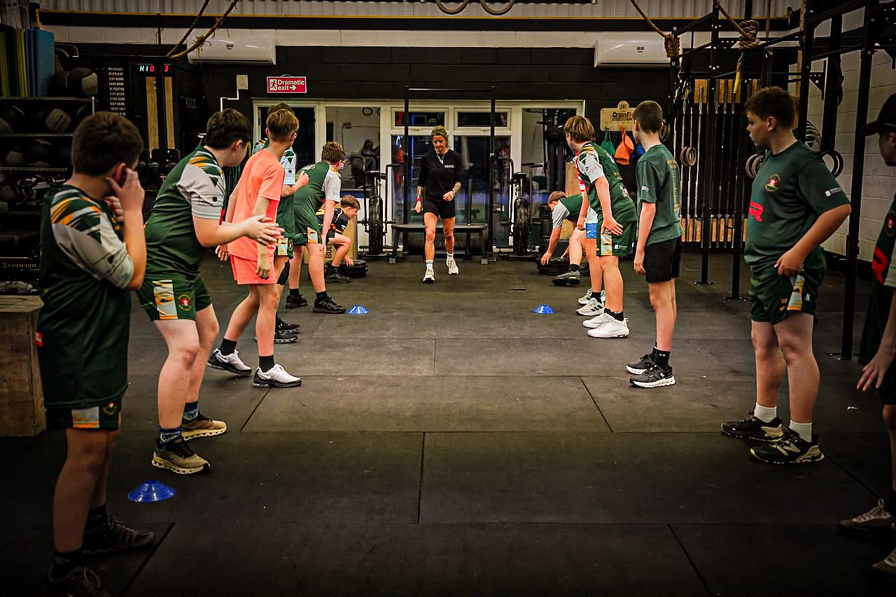 Coach Sian leading a youth rugby league squad through a warm-up drill on the gym floor